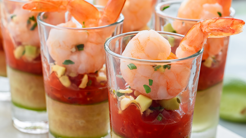 A platter of shrimp cocktail cups: cucumber rounds filled with cocktail sauce, poached shrimp, avocado and chives.