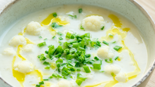 Creamy cauliflower white bean soup in a speckled ceramic bowl, garnished with chives and olive oil.