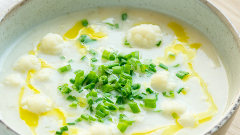 Creamy cauliflower white bean soup in a speckled ceramic bowl, garnished with chives and olive oil.