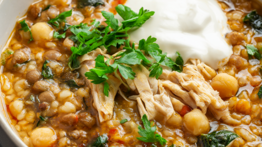 Steaming bowl of hearty lentil and chickpea soup with shredded chicken, barley, spinach, parsley and a swirl of Greek yogurt.