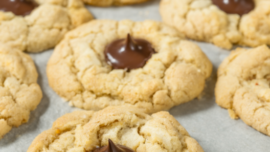 Peanut butter blossom cookies with chocolate kisses on a parchment-lined baking sheet.
