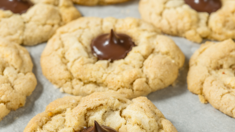 Peanut butter blossom cookies with chocolate kisses on a parchment-lined baking sheet.