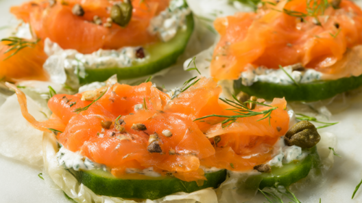 Cucumber rounds topped with dill cream cheese, smoked salmon ribbons and capers on a marble platter