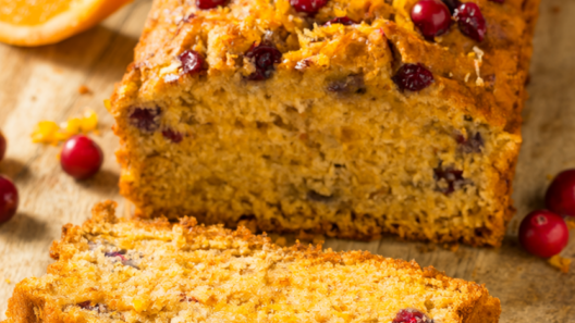 Cranberry orange quick bread loaf on a wooden board with fresh cranberries and orange zest.