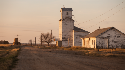 A lone white tavern with peeling paint on an empty dirt main street in the Nebraska prairie at golden hour, hay bales and a grain elevator in the distance.