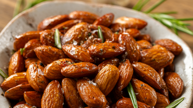 Golden roasted almonds with rosemary, garlic, and sea salt in a rustic ceramic bowl on a wooden table.