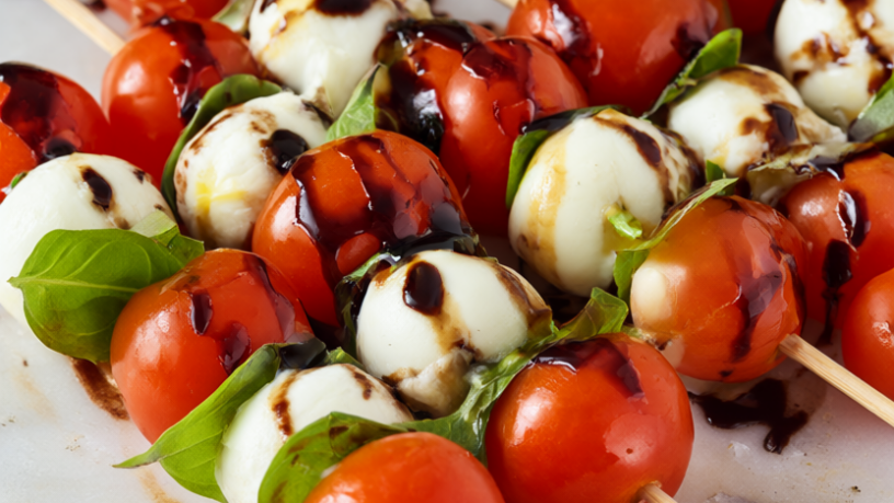 Caprese skewers with balsamic glaze: cherry tomatoes, mozzarella and basil on wooden skewers.