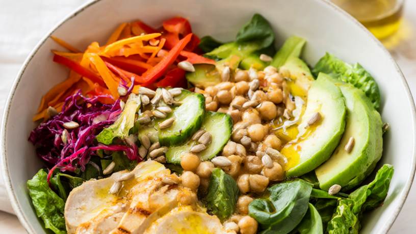 Lunch salad bowl with romaine, spinach, grilled chicken, chickpeas, cucumber, carrot, red pepper, cabbage, avocado, sunflower seeds, and vinaigrette.