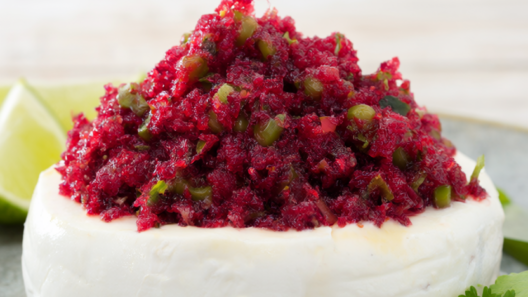 Fresh cranberry salsa with jalapeño and cilantro spooned over a round of cream cheese, garnished with lime wedges on a light wood table.