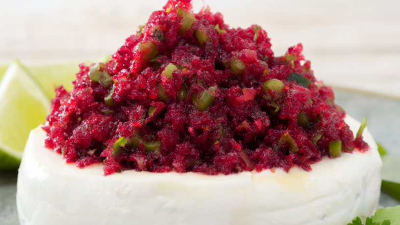 Fresh cranberry salsa with jalapeño and cilantro spooned over a round of cream cheese, garnished with lime wedges on a light wood table.